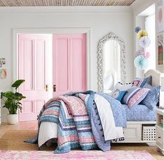 a bedroom with pink doors and bedding on the floor next to a dresser, mirror and potted plant