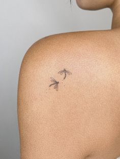 the back of a woman's shoulder with small tattoos on her left arm and two dragonflies