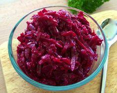 a glass bowl filled with beets on top of a wooden cutting board next to a spoon