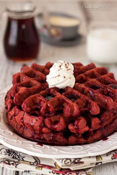 red velvet waffles on a white plate with whipped cream and chocolate syrup in the background