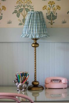 a lamp sitting on top of a glass table next to a phone and pencils