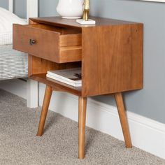 a nightstand with a lamp on top of it next to a white vase and bed