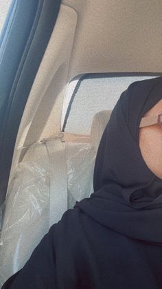 a woman sitting in the back seat of a car wearing a hijab and holding a cell phone to her ear