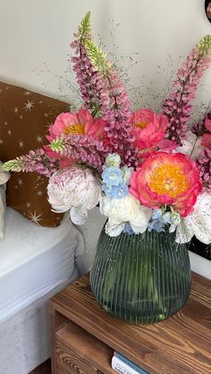 a vase filled with flowers sitting on top of a wooden table next to a bed