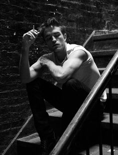 a young man sitting on the steps in front of a brick wall with his hand on his head