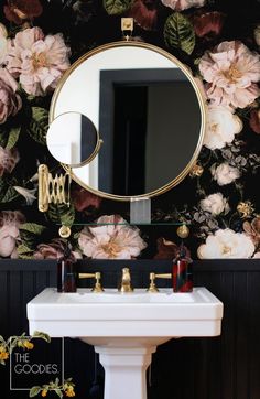 a white sink sitting under a mirror next to a wall mounted faucet with flowers on it