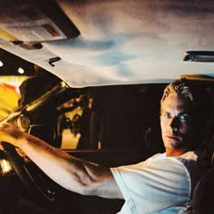 a man sitting in the driver's seat of a car with his hand on the steering wheel