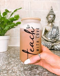 a person holding up a pink drink in front of a buddha statue and potted plant