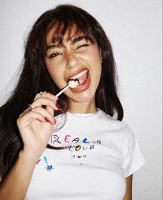 a woman brushing her teeth while wearing a white t - shirt with writing on it