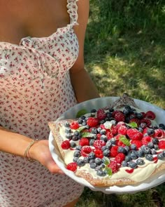 a woman holding a pie with berries and cream on it in her hands while wearing a dress