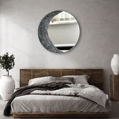 a bed sitting under a round mirror next to a vase with a plant in it