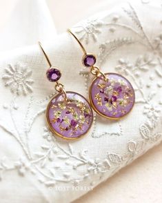 purple and gold dangle earrings with flowers on the front, sitting on a white lace doily