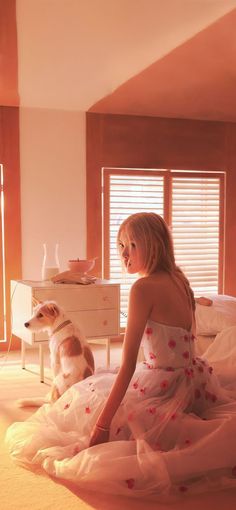 a woman in a dress sitting on a bed next to a dog