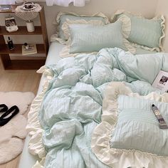 an unmade bed with blue and white comforter, pillows, and slippers