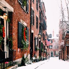 a snowy street with red brick buildings and wreaths hanging on the windows, along with snow covered sidewalks