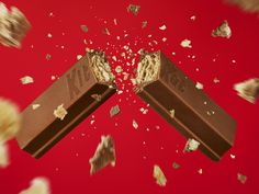 two pieces of chocolate falling into each other on a red background with scattered confetti