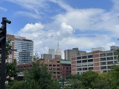 the city is full of tall buildings and lots of trees in the foreground, with a blue sky filled with white clouds