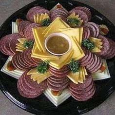 a black plate topped with lots of food on top of a white tablecloth next to a fork and knife