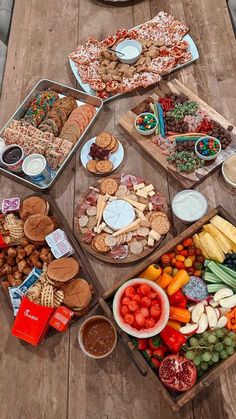 several trays filled with different types of food on a wooden picnic table, including crackers and vegetables