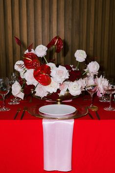 a red table cloth with white flowers and wine glasses on it is set for a formal dinner