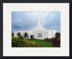 a white building with a steeple on top and flowers in the foreground against a cloudy sky