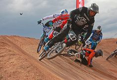 a group of people riding bikes on top of a dirt hill in the middle of an obstacle course