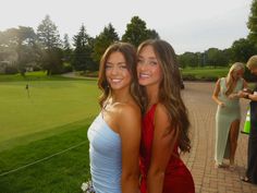 two young women standing next to each other in front of a green field and trees