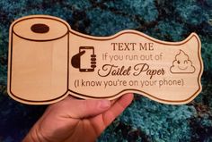 a hand holding a wooden sign that says text me if you run out of toilet paper i know you're on your phone