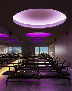 rows of treadmills in a gym with purple lighting on the ceiling and large windows