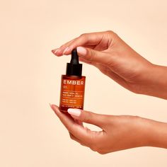 A woman’s hands holding a bottle of Ember's Jojoba + Argan Facial Oil, a pure daily support formula from two synergistic plant oils. This silky, golden emollient is non-comedogenic, and provides natural oil control, leaving you glowing throughout the day. Organic Argan Oil, Modern Packaging, Natural Preservatives, Facial Massage, Oil Control Products