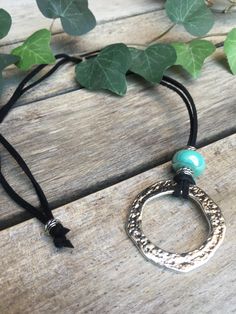 a necklace with a silver ring and turquoise beads on a wooden table next to leaves