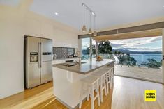 a kitchen with an island, refrigerator and sink next to a sliding glass door that looks out onto the water