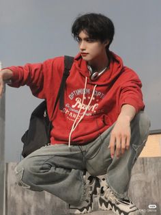 a young man sitting on top of a cement wall with his hand in his pocket