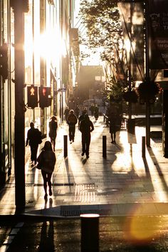 people are walking down the sidewalk in the city at sundown on a sunny day