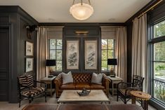 a living room filled with lots of furniture next to two large windows covered in curtains