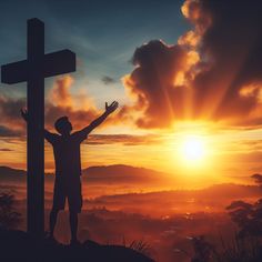 a man standing at the top of a hill with his arms raised in front of a cross