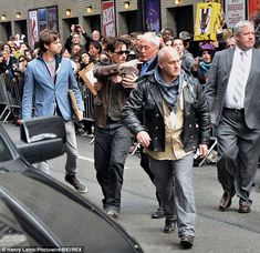 many people are walking down the street in front of some cars and onlookers