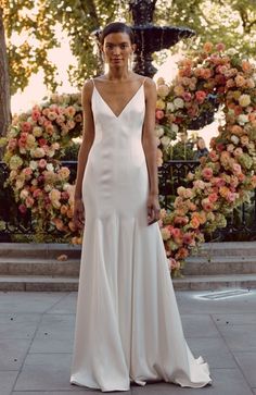 a woman standing in front of a fountain wearing a white dress