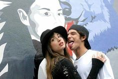 two people standing next to each other in front of a mural