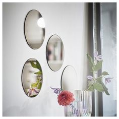 three circular mirrors hanging on the wall above a vase with flowers in it and a pink flower