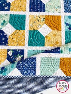 a blue and yellow quilt on top of a table cloth with the words, busy quilts