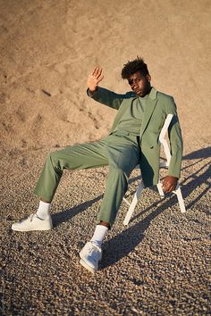 a man in a green suit sitting on a white chair and posing for the camera