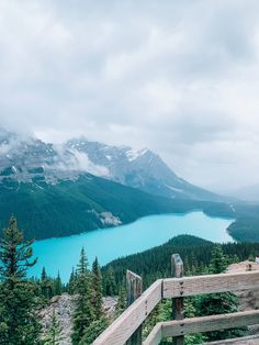 a wooden railing overlooks a mountain lake and mountains in the distance with clouds overhead