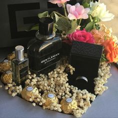 an assortment of perfumes and flowers on a gray tablecloth with black box in the middle