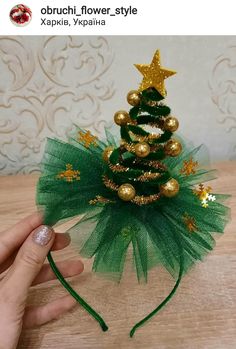 a hand is holding a small green christmas tree with gold ornaments on the top and bottom