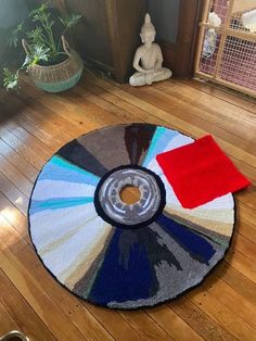 a multicolored round rug on the floor in front of a small buddha statue