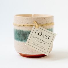 a ceramic candle holder with a tag on the front that says coast, against a white background