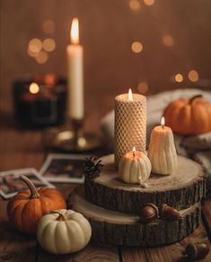 three candles sitting on top of a wooden table next to pumpkins and acorns