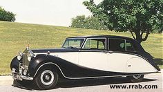 an old black and white car is parked on the side of the road in front of some trees