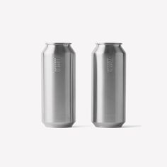 two cans of beer sitting next to each other on a white surface, one is empty and the other has no lid